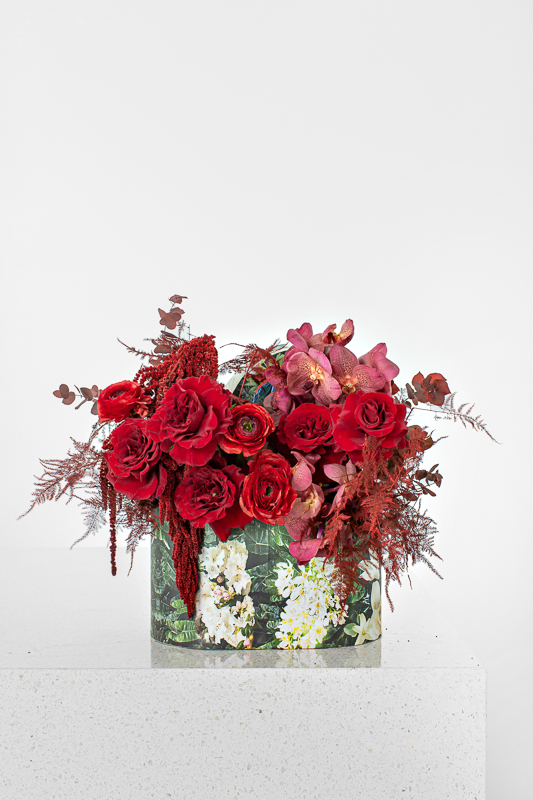 Mix of red flowers with ranunculus, roses and vanda orchids in a Bliss mini oval box